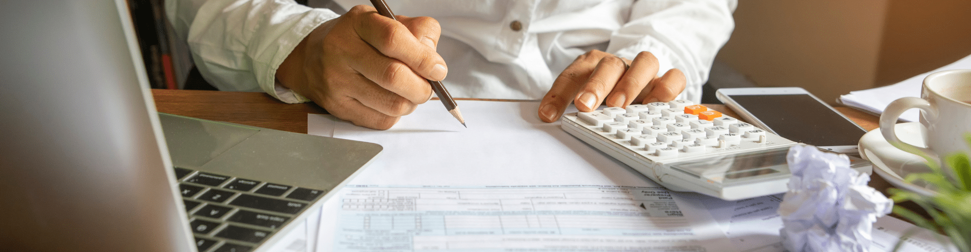 Person reviewing financial documents with a calculator and laptop, symbolizing tax preparation or financial planning.